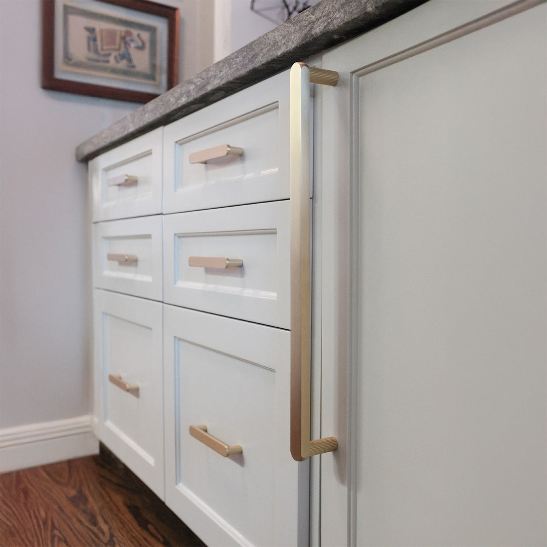 Satin brass dishwasher appliance pull on white shaker drawers and cabinets in the kitchen